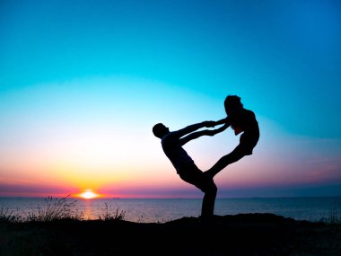 Genç kadın ve gün batımında deniz plaj üzerinde çift yoga yaparken adam silüeti. Meditasyon. Çift pratik acro yoga. Esneklik egzersiz doğa arka plan.