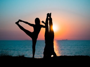 Genç kadın ve gün batımında deniz plaj üzerinde çift yoga yaparken adam silüeti. Meditasyon. Çift pratik acro yoga. Esneklik egzersiz doğa arka plan.