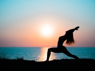 Genç kızı pratik yoga okyanus veya deniz karşı dağda gündoğumu zaman ince. Muhteşem günbatımı ışınlarının kadın silüeti.