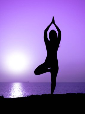 Genç kızı pratik yoga okyanus veya deniz karşı dağda gündoğumu zaman ince. Harika gün batımı mor ışınları kadın silüeti.