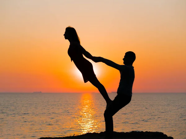 Silueta de mujer joven y hombre haciendo yoga en pareja en la playa del mar al atardecer. Meditación. Pareja practicando acro yoga. Ejercicio de flexibilidad en el entorno natural . — Foto de Stock