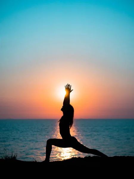 Маленькая стройная девочка практикует йогу на горе против океана или моря на восходе солнца. Силуэт женщины в лучах удивительного заката . — стоковое фото
