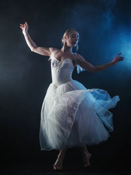 Ballerina übt ihre Bewegungen im dunklen Studio. junges Mädchen, das mit luftweißem Kleid Tutu tanzt, sich dreht und lächelt. Anmut und Zärtlichkeit in jeder Bewegung — Stockfoto