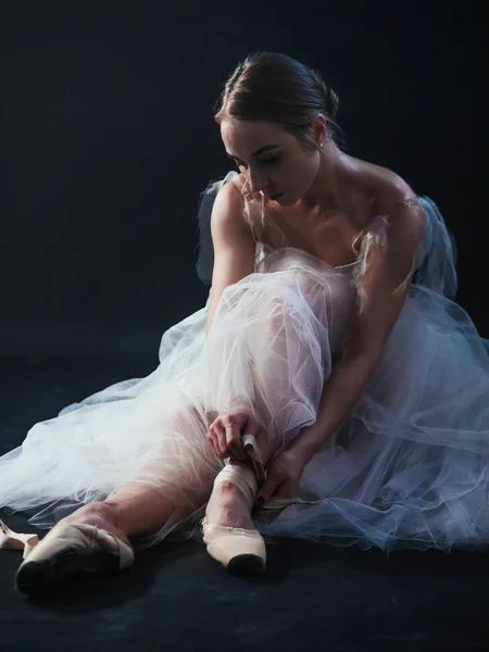 La donna corregge le scarpe da punta. Ballerina sta esercitando le sue mosse in uno studio buio. Grazia e tenerezza in ogni movimento — Foto Stock