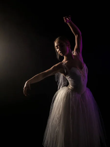 Ballerina is beoefenen haar beweegt in donkere studio. Jong meisje dansen met lucht witte jurk tutu, ronddraaien en glimlachen. Gratie en tederheid in elke beweging — Stockfoto