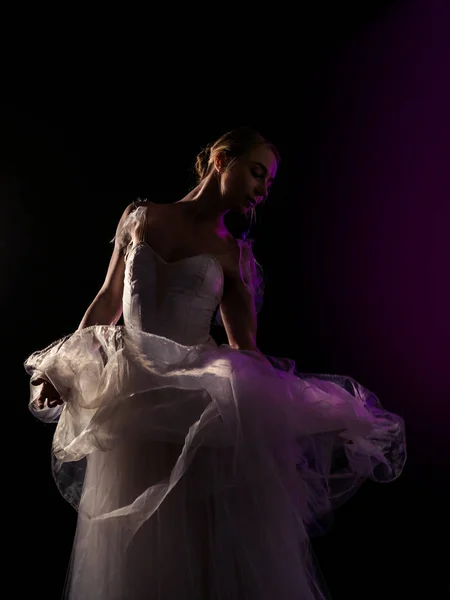 Витончена балерина в білій сукні, що танцює елементи класичного або сучасного балету в темряві з неоновим світлом і димом на чорному тлі. концепція мистецтва . — стокове фото