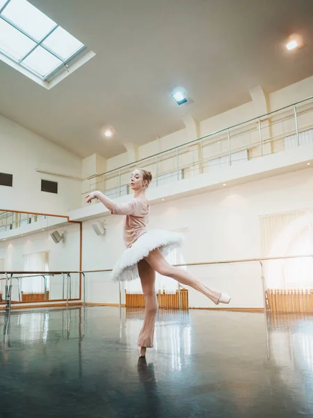 Young attractive blonde woman in white tutu clothing practicing in classical ballet in the gym. Minimalism interior, dancing sensual dance.