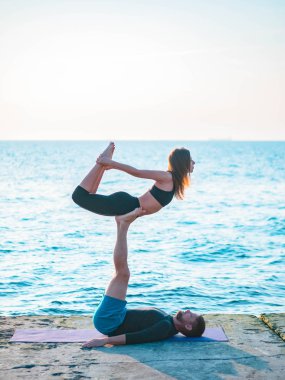 Genç güzel çift suya yakın deniz sahilde acro yoga uygulamak. Erkek ve kadın her gün pratik doğa arka plan üzerine açık yapıyor. Sağlıklı yaşam konsepti.