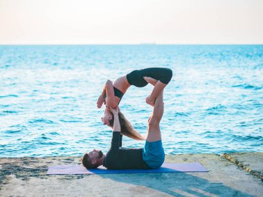 Genç güzel çift suya yakın deniz sahilde acro yoga uygulamak. Erkek ve kadın her gün pratik doğa arka plan üzerine açık yapıyor. Sağlıklı yaşam konsepti.