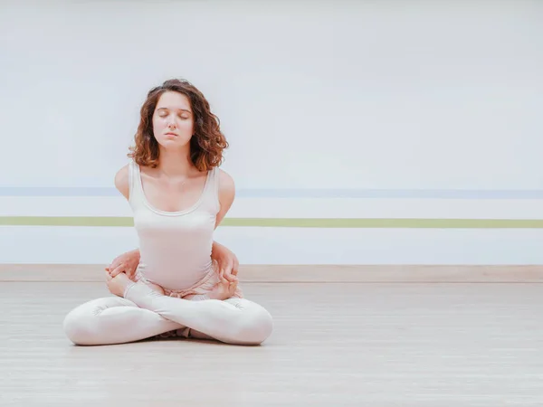 Joven mujer bonita practicando yoga en la sala de clase de estudio minimalista de luz. Chica atractiva se sienta en posición de loto clásico y comienza su meditación — Foto de Stock
