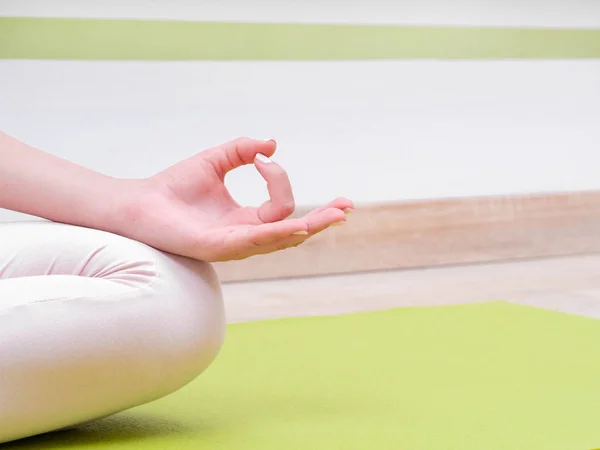 Mujer joven en mono beige sentada en una esterilla verde y practicando yoga en la sala de clases de estudio de luz. Meditando en pose de loto con Jnana Gian mudra. Om. Copiar espacio — Foto de Stock