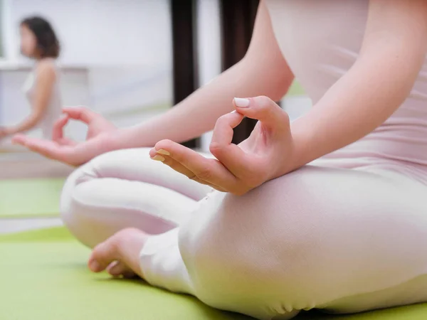 Mujer joven en mono beige sentada en una esterilla verde y practicando yoga en la sala de clases de estudio de luz. Meditando en pose de loto con Jnana Gian mudra. Om. . — Foto de Stock