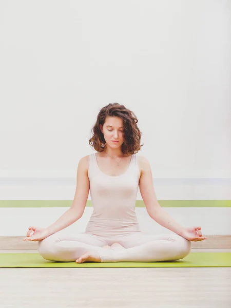 Junge hübsche Frau beim Yoga in einem minimalistischen Studio. attraktives Mädchen sitzt in klassischer Lotusposition und beginnt ihre Meditation — Stockfoto