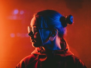 Gece şehir parlayan kırmızı neon yakınındaki sıradışı saç modeli ile bin yıllık güzel kız. Mavi boyalı saç örgü içinde. Gizemli hipster genç gözlük. Işığın yansıması.