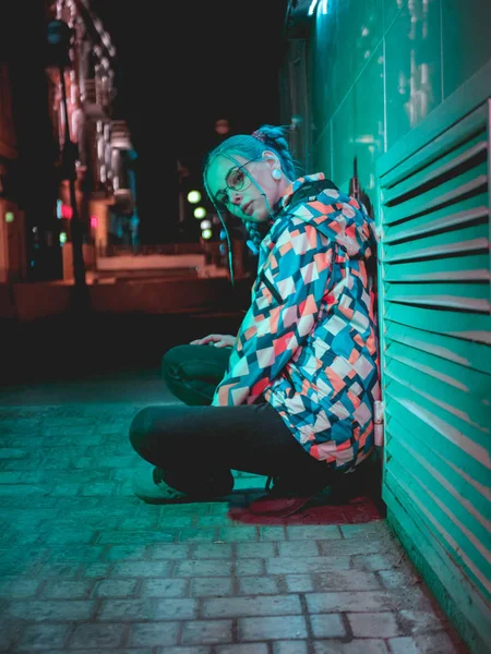 Menina bonita nova com penteado incomum perto de luz de néon turquesa brilhante da cidade à noite. Cabelo azul tingido em tranças. Pensivo hipster adolescente em óculos . — Fotografia de Stock