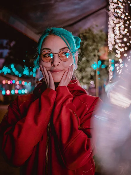 Gadis cantik dengan warna biru rambut yang tidak biasa, kacamata transparan, menusuk berdiri di jalan malam dengan latar belakang lampu neon. Potret remaja lucu yang bahagia gaya . — Stok Foto