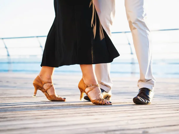 Young attractive couple dancing latin bachata near sea or ocean. Sunlight background. Summer time, romantic scene. Legs of professional dancers.
