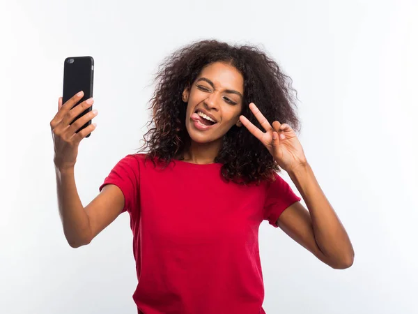 Kırmızı t-shirt yapımı selfie resmi smartphone için mutlu genç Afro-Amerikan kız beyaz arka plan üzerinde gülümseyen. Teknoloji kavramı. — Stok fotoğraf