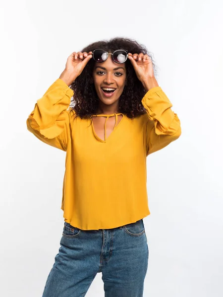 Schöne afrikanisch-amerikanische Frau mit Afro-Haaren in gelber Kleidung und Sonnenbrille, die vor weißem Hintergrund in die Kamera lächelt. Niedliche Mixed Race Girls Portrait mit Erstaunen — Stockfoto