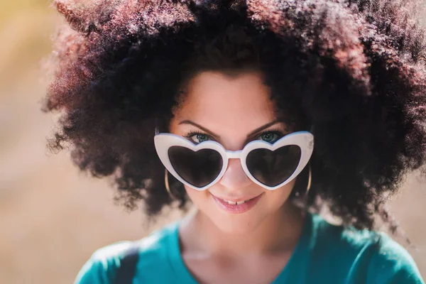 Portret zmysłowy młoda ładna kobieta z afrykańskich fryzury kręcone i okulary przeciwsłoneczne. Piękna dziewczyna z zielonymi oczami, uśmiechając się do kamery w lato na zewnątrz. — Zdjęcie stockowe