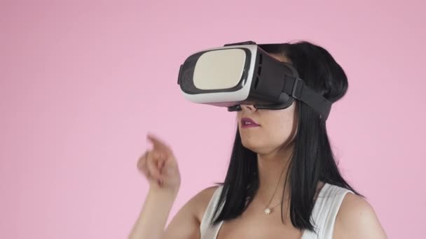 Bella donna che tocca l'aria durante l'esperienza VR isolato sul rosa. Ragazza utilizzando auricolare realtà virtuale . — Video Stock