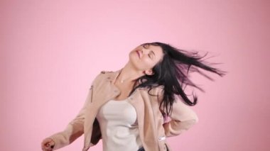 Genç güzel pembe ceket dans ifade kız. Moda modeli esmer saçlar ile renkli arka plan üzerinde stüdyoda cesedi taşımak. Ağır çekim