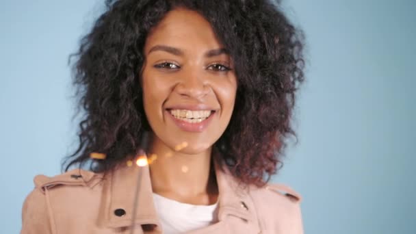 향 및 벵골 화재와 함께 축 하 하는 핑크 가죽 자 켓에 아프리카계 미국인 여자. 행복 한 혼합 인종 여자 웃 고 파란색 배경 재미. 슬로우 모션 — 비디오