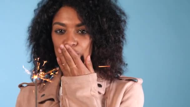 Csillogó bengáli tűz afro-amerikai womans kezét a kék háttér. Karácsonyi ünnep fogalma. Fiatal csinos lány afro frizura ünnepli, mosolyog, élvezi időt. — Stock videók