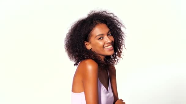 Ελκυστική αφρικανική αμερικανική γυναίκα με τα Άφρο μαλλιά στο ροζ κορυφή χαμόγελο, το φλερτ σε φωτογραφική μηχανή πάνω από το φόντο λευκό τοίχο. Πορτραίτο κορίτσια χαριτωμένα μικτή φυλή. Έννοια της υγείας. — Αρχείο Βίντεο