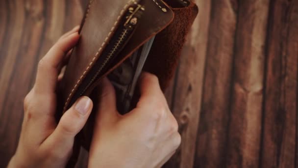 Bovenaanzicht van een vrouw die tellen en neemt dollar uit haar portemonnee van bruin leer. Vrouw houdt de beurs tegen houten achtergrond. Slow motion — Stockvideo