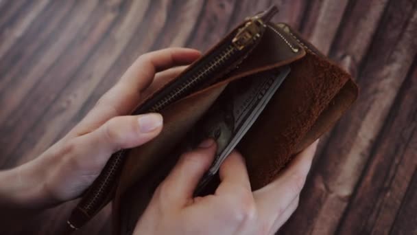 Widok z góry kobiety liczenia i odbywa się dolarów z jej brązowy skórzany portfel. Kobieta trzyma torebkę tle drewnianych. Zwolnionym tempie. — Wideo stockowe
