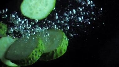 Sıçramasına ve siyah arka plan üzerine, ağır çekim düşen suya salatalık dilimleri.