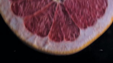 Patlayıcı çarpıcı sıçrama ile şeffaf suya dalan yuvarlak taze sulu greyfurt dilim. Sualtı yüksek hızlı yavaş hareket siyah arka plan üzerine vurdu. İzole pomelo.