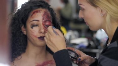 Makyöz makyaj kız halloween olun stüdyoda. Cadılar Bayramı yüz sanat. Kadın profesyonel yağlıboya İspanyol kız yüzünde geçerlidir. Savaş-boya kan, yaralar ve yaralar. Ağır çekim.
