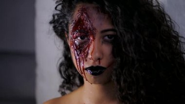 Cadılar Bayramı kan makyaj kızla Genç zombi korkunç portresi. Güzel latin kadın kamera Studio bakarak kıvırcık saçlı. Ağır çekim.