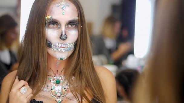 Mladá dívka s výtvarným obličej halloween při pohledu do zrcadla odraz v šatně. Portrét okouzlující lebka s kamínky a flitry. Profesionální make-up pro oslavu — Stock video
