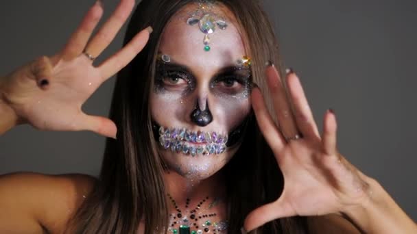 A menina com arte de cara de halloween criativa assusta no estúdio. Retrato assustador de crânio glamouroso com strass e lantejoulas. Maquiagem profissional para a celebração. Movimento lento . — Vídeo de Stock