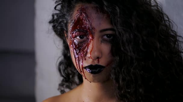 Portrait effrayant de jeune fille zombie avec maquillage de sang Halloween. Belle femme latine avec les cheveux bouclés regardant dans la caméra en studio. Mouvement lent . — Video