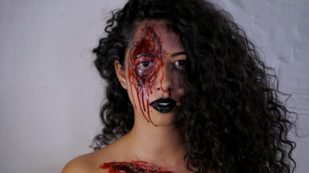 Retrato assustador de jovem assassina com maquiagem de sangue de Halloween. Mulher latina bonita com cabelo encaracolado olhando para a câmera no estúdio. Movimento lento . — Vídeo de Stock