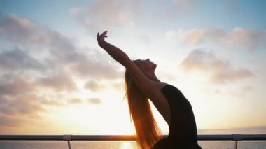 Ağır çekim. Güzel balerin performans gösteren tek ayak üzerinde dönüş. Sarışın kadın dolgu gündoğumu okyanus ya da deniz kumsalda yukarıda üzerinde siyah Bale tutu. Kadın kolları ile dans.