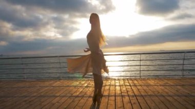 Balerin bej ipek elbise ve pointe setin okyanus ya da deniz plaj yukarıda güneş doğarken dans. Güzel sarışın genç kadın uzun saçlı duygular ile klasik çalışmaları uygulamak.