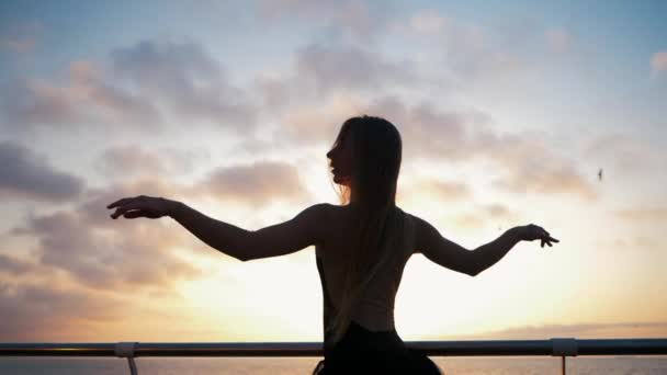 Lenteur de la motion. Belle ballerine jouant de la pirouette. Femme blonde en tutu de ballet noir sur un remblai au-dessus de l'océan ou de la plage au lever du soleil. Danse féminine avec les bras . — Video
