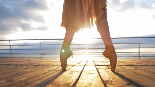 Close-up van een ballet dansers voeten als ze in pointe oefeningen aan de kade in de buurt van de zee, zonsopgang achtergrond, dames voeten in pointe-schoenen praktijken. Ballerina toont klassieke ballet pas. Slow motion. — Stockvideo