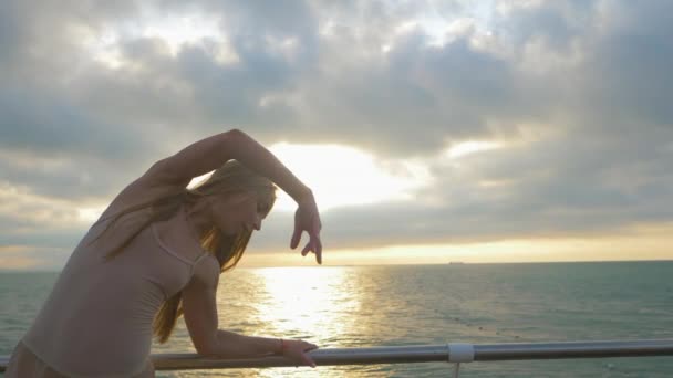 Belle scène d'une ballerine dansante en robe de soie beige et pointe sur un remblai au-dessus de l'océan ou de la plage au coucher du soleil. femme sensuelle aux cheveux longs pratiquant des étirements et des exercices classiques . — Video