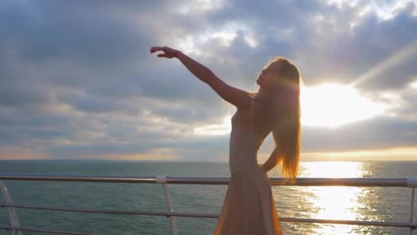 Wunderschöne Szene einer tanzenden Ballerina in beigem Seidenkleid und Spitze auf einem Damm über dem Meer oder am Strand bei Sonnenuntergang. sinnliche Frau mit langen Haaren übt Stretching und klassische Übungen. — Stockvideo