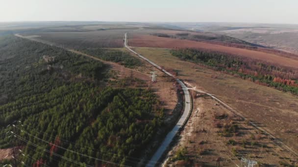 Légifelvételek az autóban vezetés országúton. Filmszerű tónusú. drone lövés repül át elektromos vezetékek és aszfaltozott út. Szép őszi szezon. Hegyek és elektromos vezetékek — Stock videók