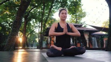 Namaste elleriyle Lotus poz oturan ve meditasyon veya dua konsantre kız. Oryantal görünüm pratik yoga yalnız tropik ada ahşap güvertesinde olan kadın