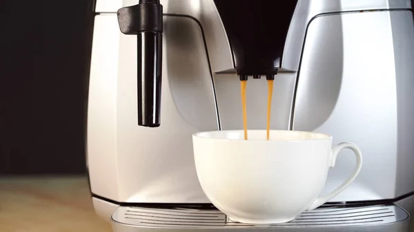 White cup of espresso pouring from professional coffee machine. Close-Up. Coffee maker. Modern technology concept