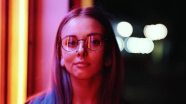 Modern kız gece parlak neon duvar yakınındaki boyalı saç modeli ile. Altın pul olarak çiller, burun piercing. Gizemli hipster genç gözlük gülümseyerek kameraya bakıyor
