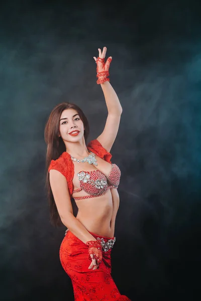 Спокуслива сексуальна традиційна дівчина танцює на фіолетовому неоновому тлі диму. Жінка в екзотичному червоному костюмі сексуально рухає її напівголим тілом . — стокове фото